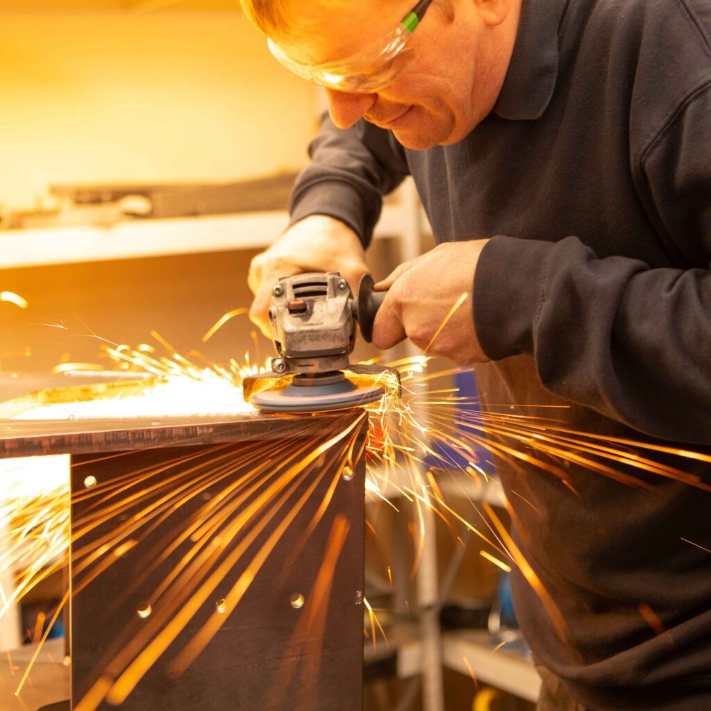 Close up of a man using a disc sander on metal with sparks flying