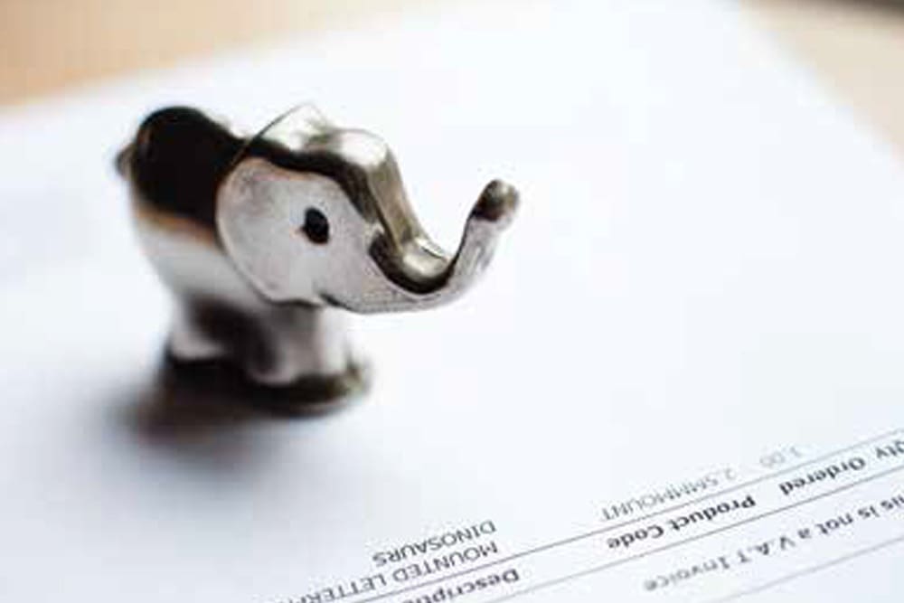 Close up photo of a small metal elephant sitting on a white sheet of paper