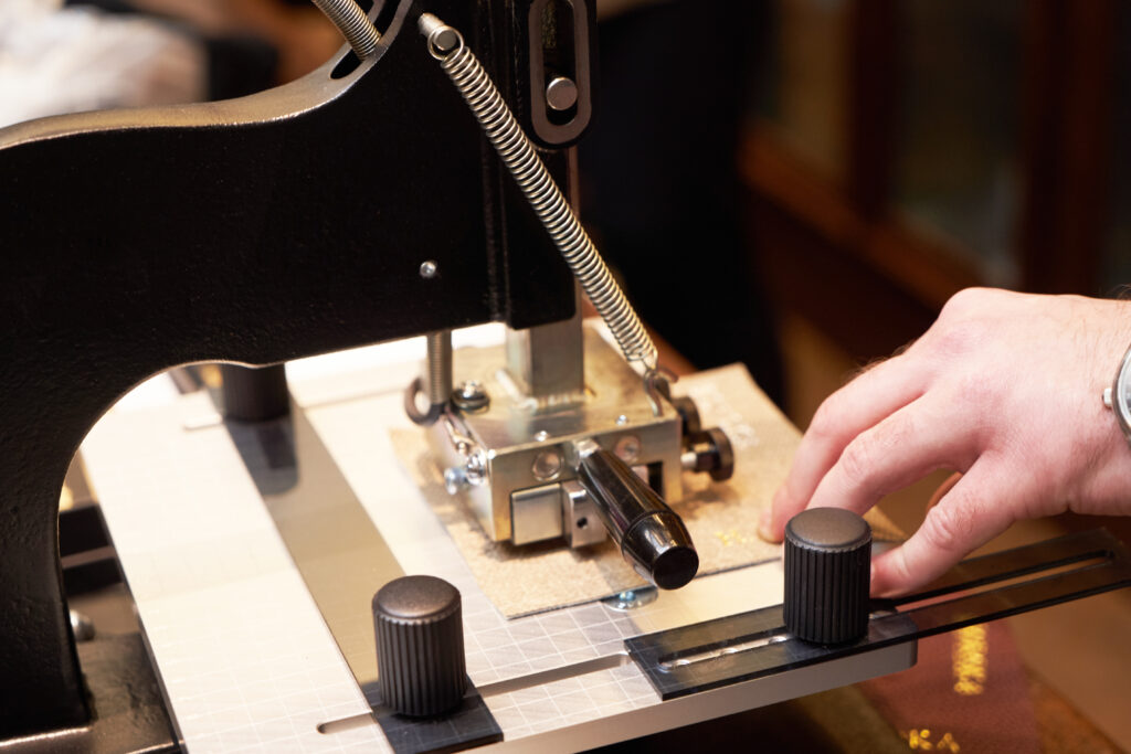 Leather crafting with iron press machine. Craftsman hands working at leather engraving machine. Working process of making leather wallet in the leather workshop, close-up