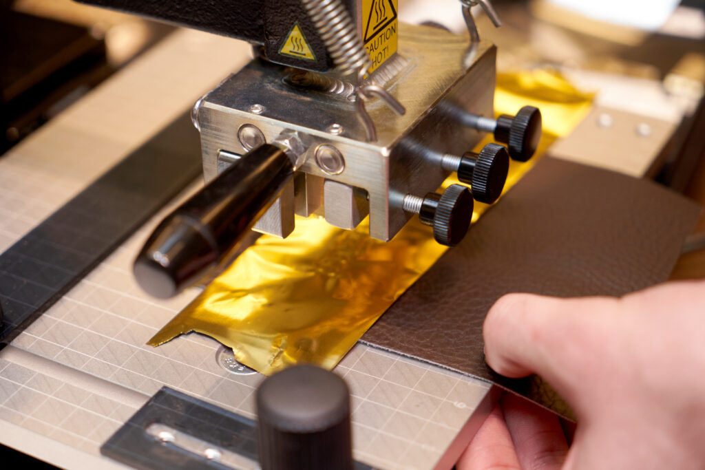 Leather crafting with iron press machine. Craftsman hands working at leather engraving machine. Working process of making leather wallet in the leather workshop, close-up
