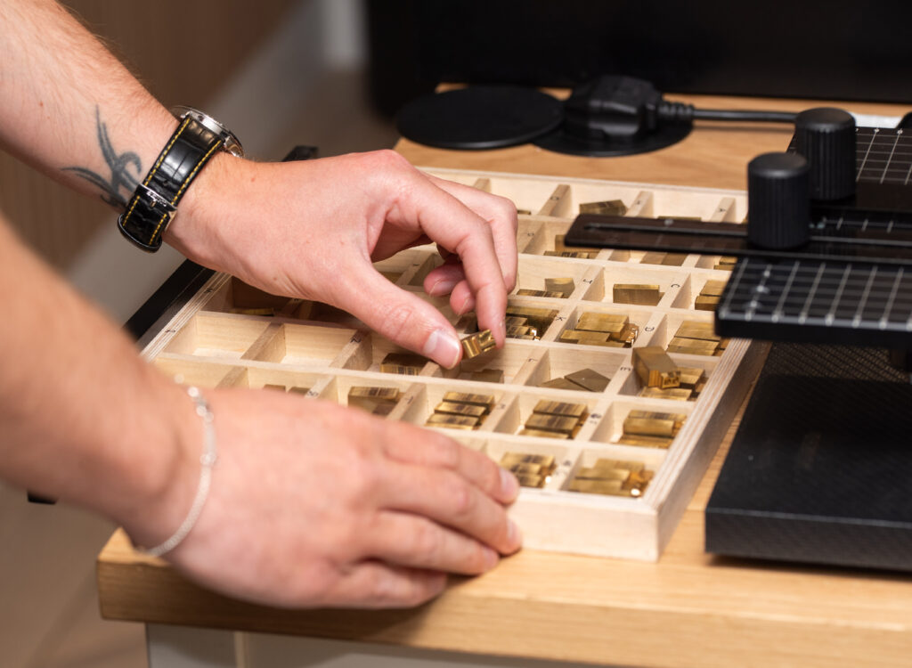 Man selecting brass type from a wooden box of various letter